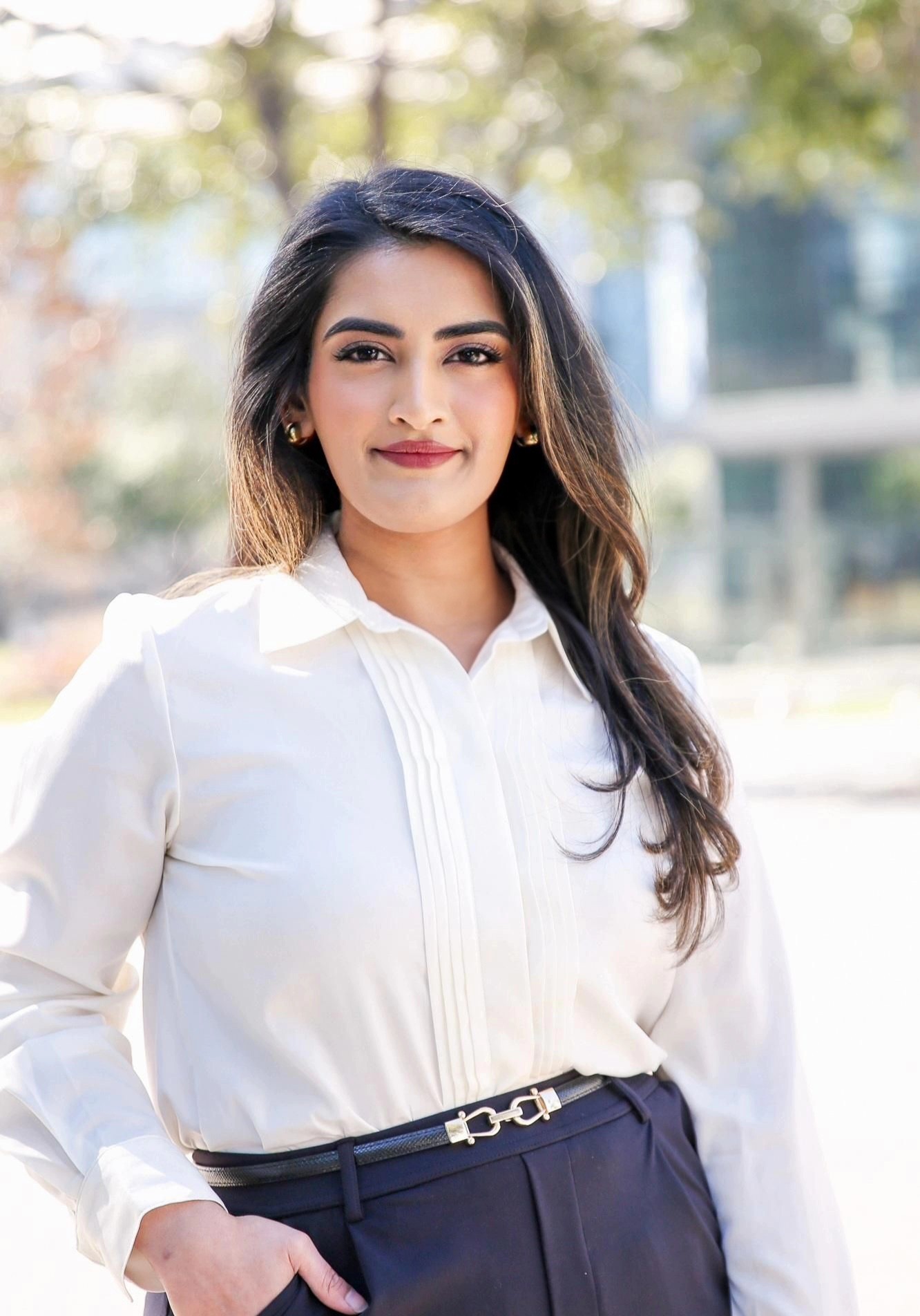 Portrait of Minna Kay outdoors, wearing a white pleated blouse and navy trousers.